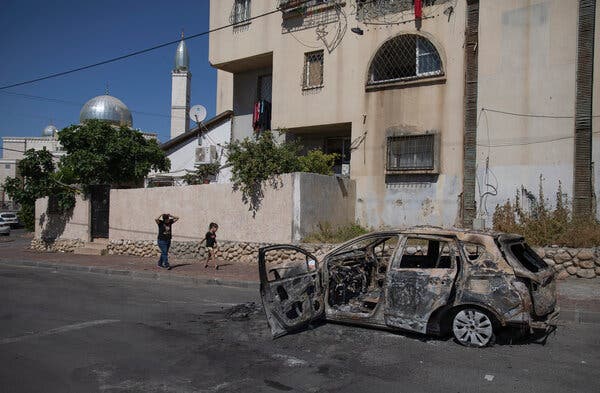 An Israeli Arab woman and her daughter walking past the wreckage of a car in Lod, Israel, on Wednesday.