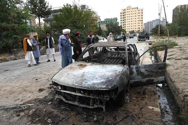 Taliban fighters investigate a burned-out car after multiple rockets were fired in Kabul, Afghanistan, on Monday.