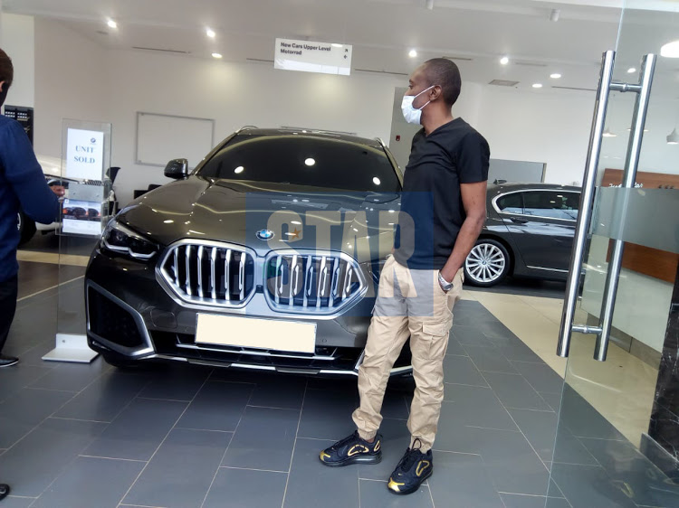 Maina Kageni standing next to his 2020 BMW X6. His collection includes several other high-end cars.