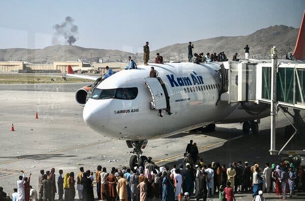 People climb atop a plane as they wait at the Kabul airport on Monday. Thousands rushed to the city’s airport trying to flee as the Taliban took control.
