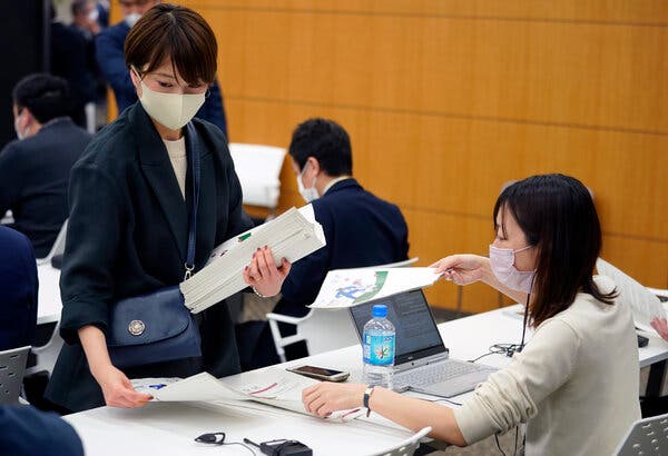 A staff member distributes the second version of the Tokyo 2020 playbook before a press briefing earlier today.