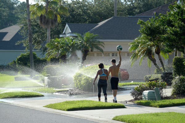 A couple walk through sprinklers in the Hunter’s Creek neighborhood in Orlando, Fla.