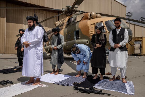 Taliban praying at the Kabul airport in Afghanistan on Tuesday, in front of an Mi-17 helicopter damaged by departing U.S. forces.